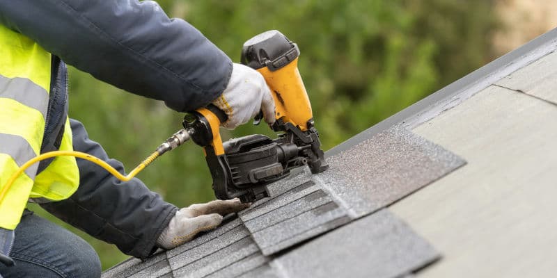 Roofer installing asphalt shingles with a pneumatic nail gun