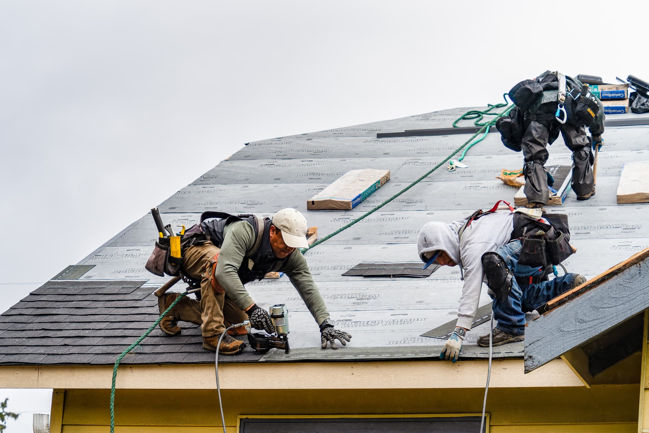 Roofing crew installing shingles over underlayment on a residential roof