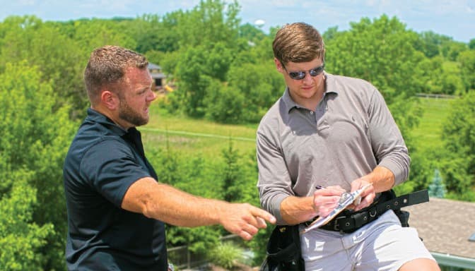 Two NextRoof 360 inspectors reviewing a roof and taking notes on a clipboard