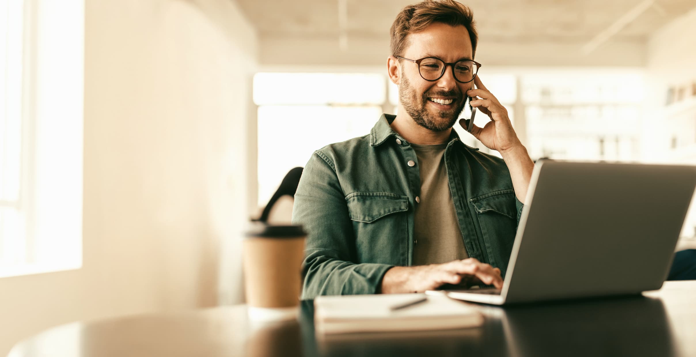 Smiling homeowner on the phone while using a laptop to reach NextRoof 360