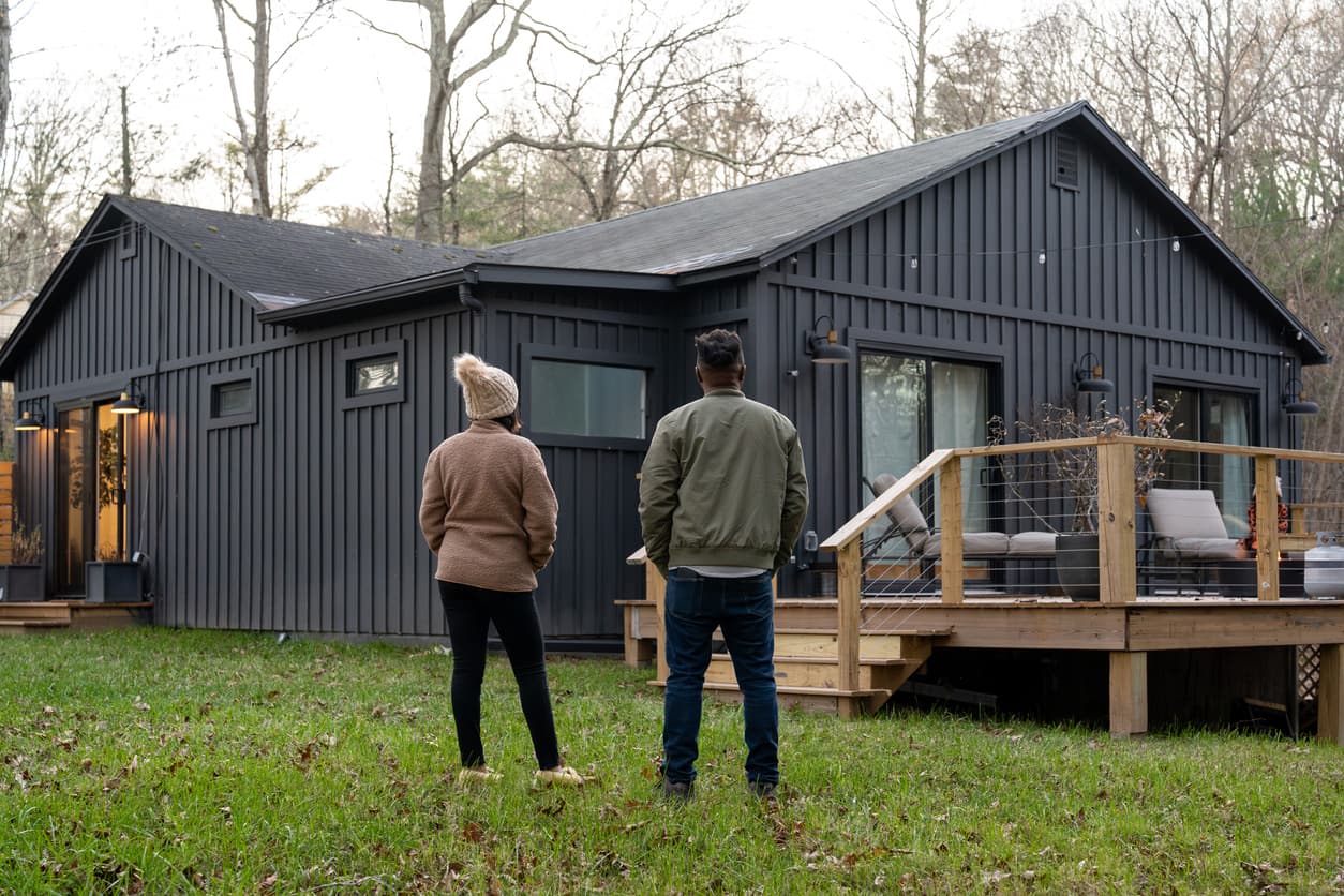 Two homeowners standing in their backyard looking at their modern dark board-and-batten home